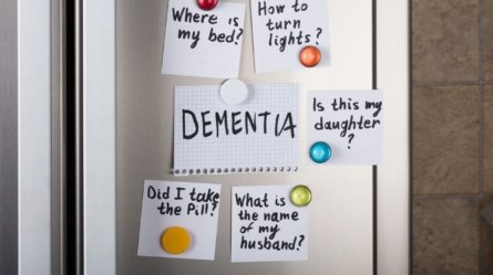 Close-up of dementia notes with various reminders attached with magnetic thumbtacks on a refrigerator.