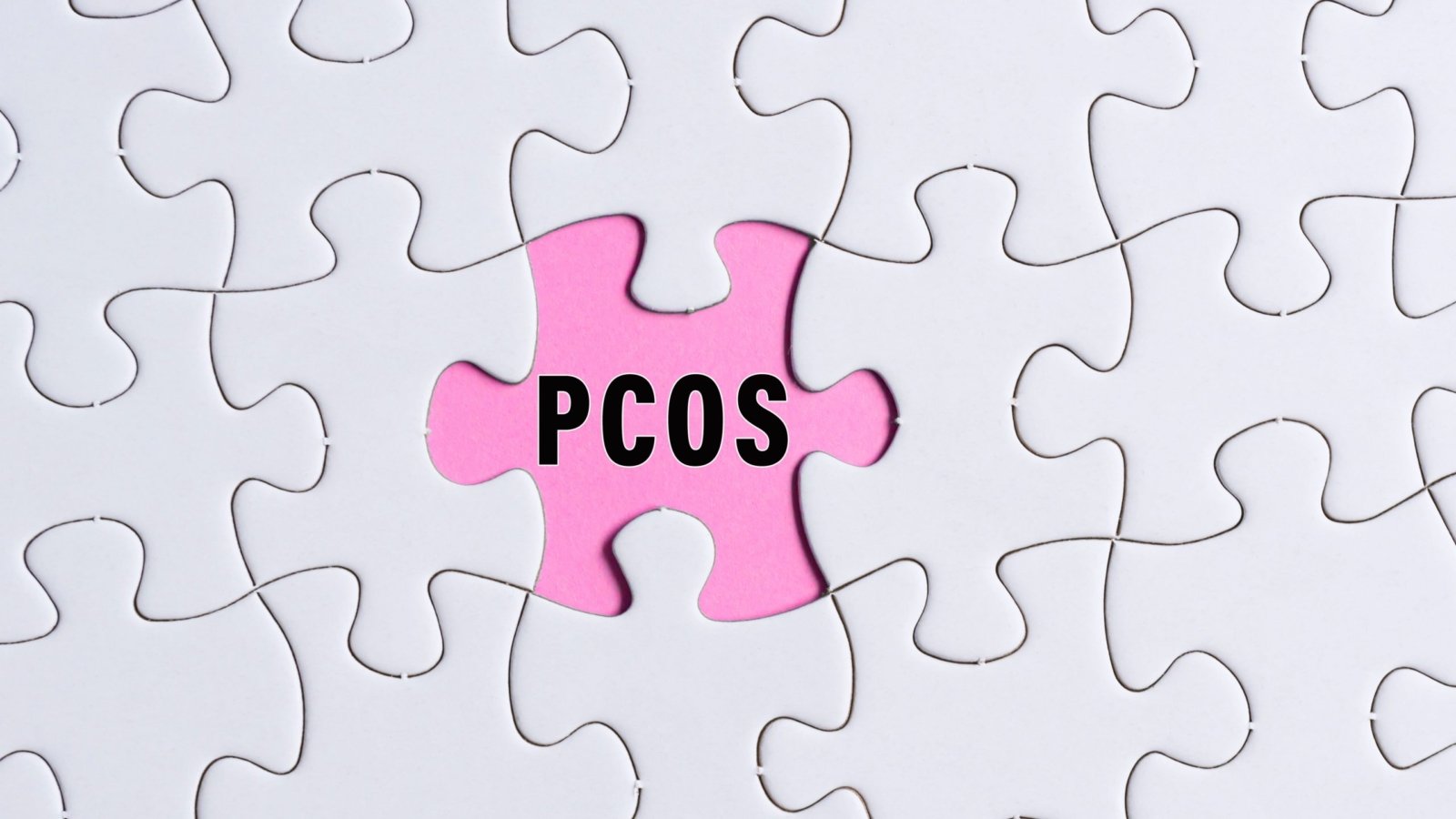 polycystic ovary syndrome (PCOS) text on white jigsaw puzzle over pink background.