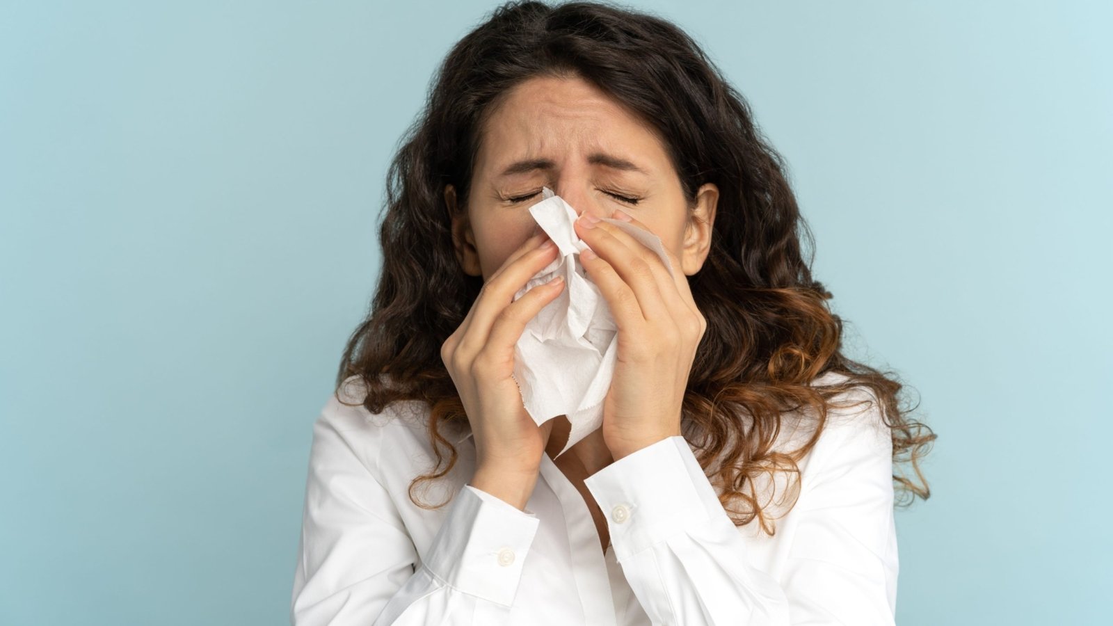 A woman sneezing into a paper tissue.