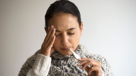 A young woman is seen to be suffering from fever and using a thermometer to know her body temperature.