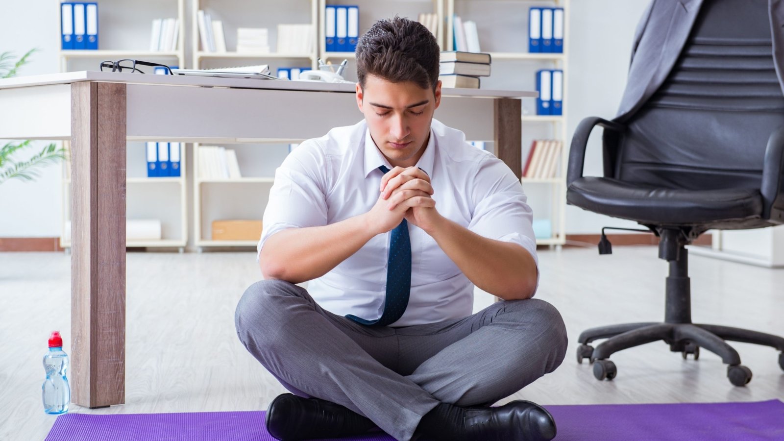 A concept image of Workplace Wellness: a man in a zen poise during a work break relaxing.