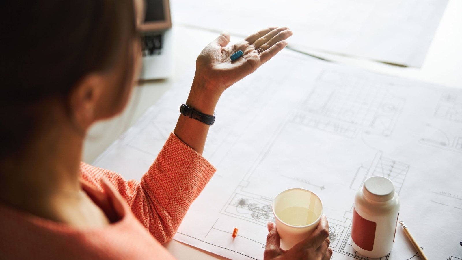 A woman in the middle of her work is seen taking a supplement to increase her Vitamin D Levels.